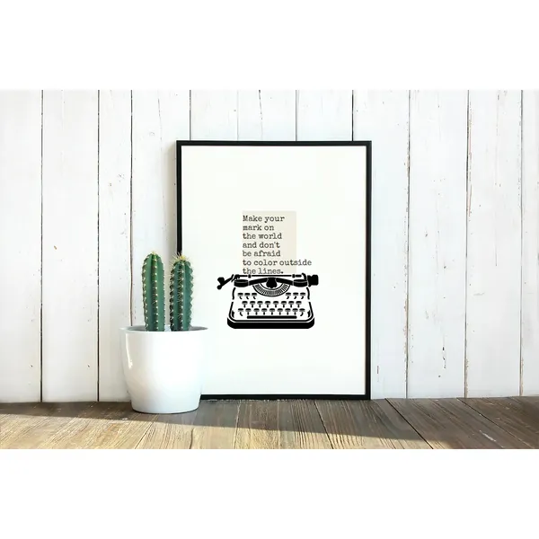 A bright scene of a stylish home has a picture as the centerpiece. The picture is placed against a wall on the ground featuring a graphic depiction of a vintage typewriter with a quote on the page. The quote is: Make your mark on the world and don't be afraid to color outside the lines. Next to the picture is a potted pair of cactuses. The wall has bright white wood panelling and dark brown wooden floor.