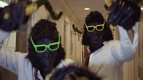 2 men dressed up as monkey in suits dancing funnily with bananas in their hands