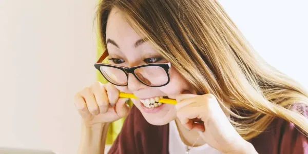 A woman is holding a pencil between her teeth and chomping down in an expressio of frustration.