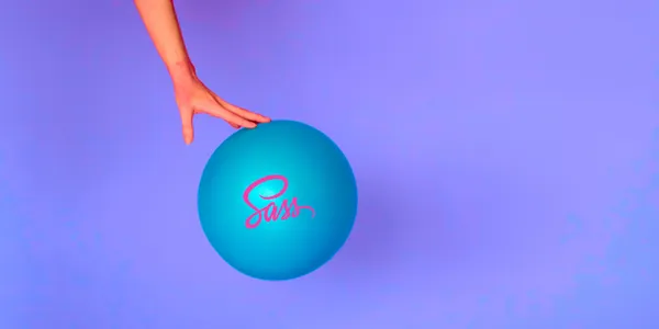 A hand is lightly holding a ball with the word Sass written on it.
